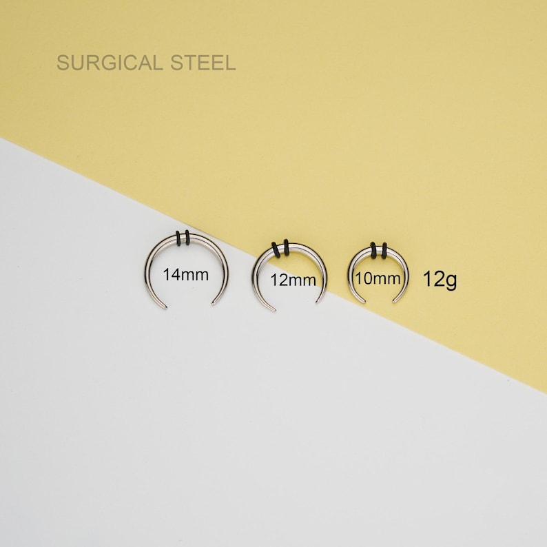 May include: Three silver surgical steel nose rings with black rubber o-rings. The rings are 14mm, 12mm, and 10mm in diameter. The rings are labeled with their size in millimeters. The text "SURGICAL STEEL" and "12g" are also visible in the image.
