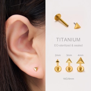 Puede incluir: Pendientes de titanio dorados con forma triangular. La imagen muestra los pendientes en tamaños de 2 mm, 3 mm y 4 mm, junto con el texto "TITANIUM" y "EO-sterilized & sealed". Un pendiente se muestra en una oreja.
