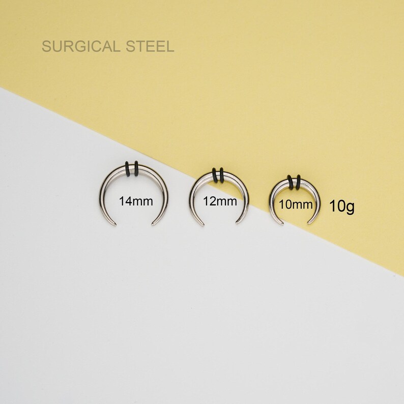 May include: Three surgical steel septum rings in different sizes: 14mm, 12mm, and 10mm. The rings are silver and have a black rubber o-ring on each side. The rings are labeled with their size in millimeters. The text "SURGICAL STEEL" is at the top of the image. The rings are on a white and yellow background.