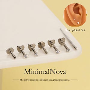 Puede incluir: Un conjunto de seis pendientes plateados con forma de corazón y gemas transparentes. La imagen incluye una oreja con un pendiente y el texto "Completed Set" y "MinimalNova".