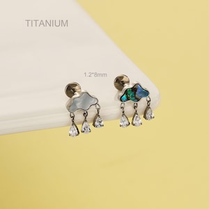 Könnte beinhalten: Titan-Ohrringe mit Wolkenmotiv und tropfenförmigen Kristallen. Die Wolken sind hellblau und schillernd. Die Ohrringe messen 1,2 mm x 8 mm.
