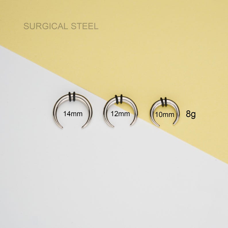 May include: Three silver surgical steel septum rings with black o-rings. The rings are 14mm, 12mm, and 10mm in diameter. The rings are labeled with their size in millimeters. The text "SURGICAL STEEL" is at the top of the image. The text "8g" is at the right side of the image.