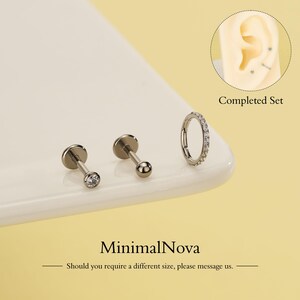 Op de afbeelding: Een set zilverkleurige lichaamsjuwelen, waaronder twee platte studs, één met een heldere edelsteen, en een oorring met kleine, heldere stenen. De afbeelding bevat de tekst "Completed Set" en "MinimalNova".