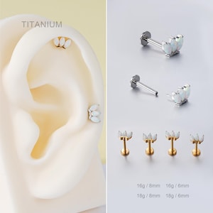 Op de afbeelding: Titanium oorbellen met een wit opaal bloemmotief. De afbeelding toont verschillende stijlen, waaronder labret- en platte achterkant studs. Maten: 16g/8mm, 16g/6mm, 18g/8mm en 18g/6mm. Het woord "Titanium" is ook zichtbaar.