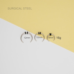 May include: Three surgical steel nose rings with black rubber stoppers. The rings are 8mm, 10mm, and 12mm in diameter. The gauge is 16g.