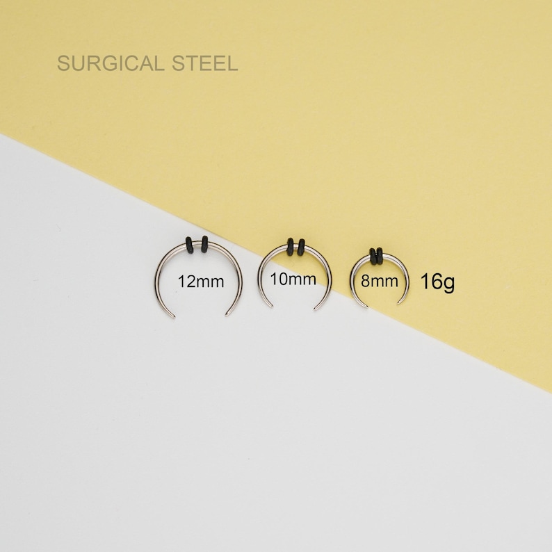 May include: Three surgical steel nose rings with black rubber stoppers. The rings are 8mm, 10mm, and 12mm in diameter. The gauge is 16g.