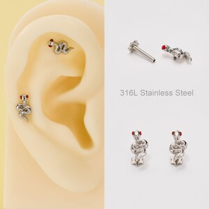 May include: Silver-colored snake-shaped earrings with red accents. The earrings are displayed on an ear model and on a white background. The text "316L Stainless Steel" is also visible.