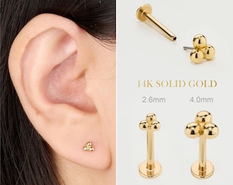 Puede incluir: Primer plano de una oreja con un pequeño pendiente de oro. El pendiente tiene un grupo de tres pequeñas cuentas redondas. Imágenes adicionales muestran el diseño del pendiente y el texto "14K SOLID GOLD" con tamaños de 2,6 mm y 4,0 mm.