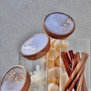 May include: Three glass jars with lids featuring a light purple and gold resin design. The jars are filled with various items, including cinnamon sticks, coconut flakes, and seashells.