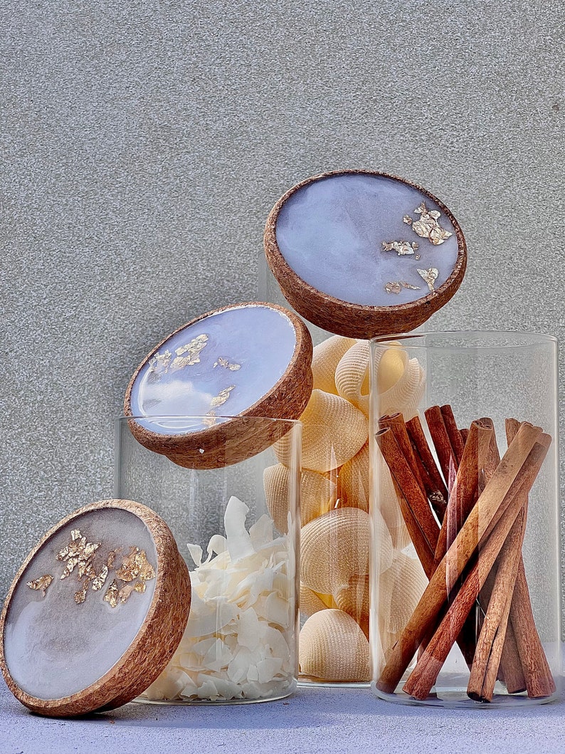 May include: Three glass jars with lids featuring a light purple and gold resin design. The jars are filled with various items, including cinnamon sticks, coconut flakes, and seashells.