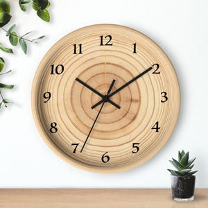 May include: A round wooden wall clock with a light brown finish. The clock face features a natural wood grain pattern with black numerals and hands. The clock is approximately 10 inches in diameter.