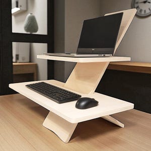 May include: A light-coloured wooden laptop stand with a keyboard and mouse. The stand has two tiers, one for the laptop and one for the keyboard and mouse. The stand is on a wooden surface.