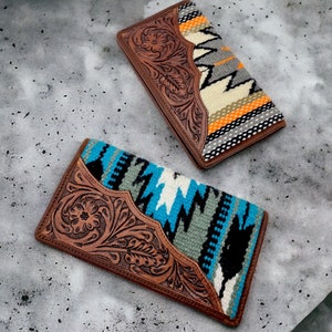 May include: Two brown leather wallets with tooled floral designs. The wallets are lined with colourful woven fabric with geometric patterns.
