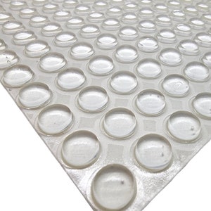 May include: A sheet of clear, round, adhesive rubber bumpers. The bumpers are arranged in a grid pattern on a white backing sheet.
