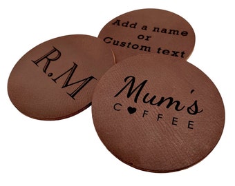 May include: Three brown leather coasters with engraved text. The first coaster says "R.M." The second coaster says "Add a name or custom text". The third coaster says "Mum's Coffee" with a small heart symbol.