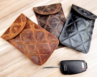 May include: Three leather phone cases with a quilted design. The cases are brown, black, and a distressed brown. A black car key with a silver key ring is in the foreground.