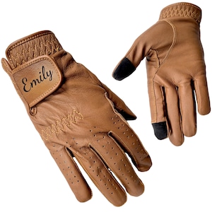 May include: A pair of brown leather golf gloves with the name "Emily" printed on the wrist strap. The gloves have perforations for breathability and black touch screen fingertips. The stitching is a lighter brown.