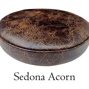May include: A brown leather stool with a distressed finish. The stool is round and has a slightly raised edge. The text "Sedona Acorn" is printed below the stool.