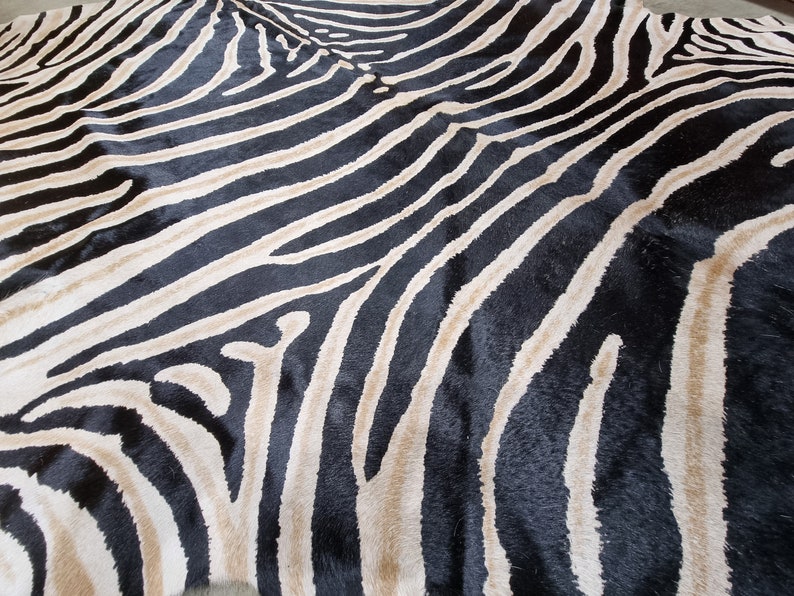 Pode incluir: Um grande tapete com listras de zebra com textura de pele natural. O tapete apresenta listras pretas e brancas arrojadas, criando um padr&atilde;o marcante. A pele parece ser costurada no centro. O tapete &eacute; adequado para uma sala de estar ou quarto.