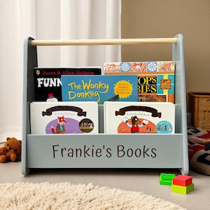 May include: A light blue wooden bookshelf with a natural wood handle, holding several children's books. The text "Frankie's Books" is printed on the front. Books include "The Wonky Donkey" and "FUNN".