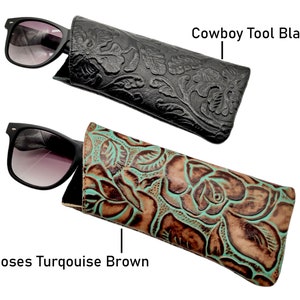 May include: Two different styles of leather sunglass cases. The first case is black with an embossed floral design and the text "Cowboy Tool Black". The second case is brown with a turquoise floral design and the text "Roses Turquoise Brown".