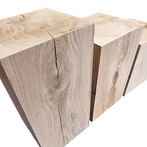 May include: Four wooden blocks stacked in a staggered formation, showcasing the natural grain and knots of the wood. The blocks are light brown in color and have a rough, unfinished texture.