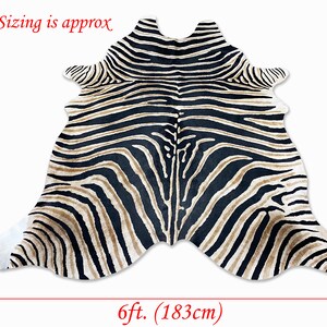 Pode incluir: Tapete com listras de zebra com listras pretas e bege. O tapete tem aproximadamente 213 cm de comprimento e 183 cm de largura. O tapete tem uma forma irregular, assemelhando-se a uma pele de zebra. O texto "Sizing is approx" &eacute; vis&iacute;vel.