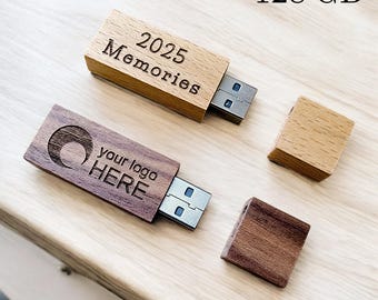 May include: Two wooden USB flash drives, one light-colored and one dark-colored, with their caps off. The light-colored drive has the text "2025 Memories" engraved on it. The dark-colored drive has the text "your logo HERE" engraved on it. The text "128 GB" is in the top right corner.
