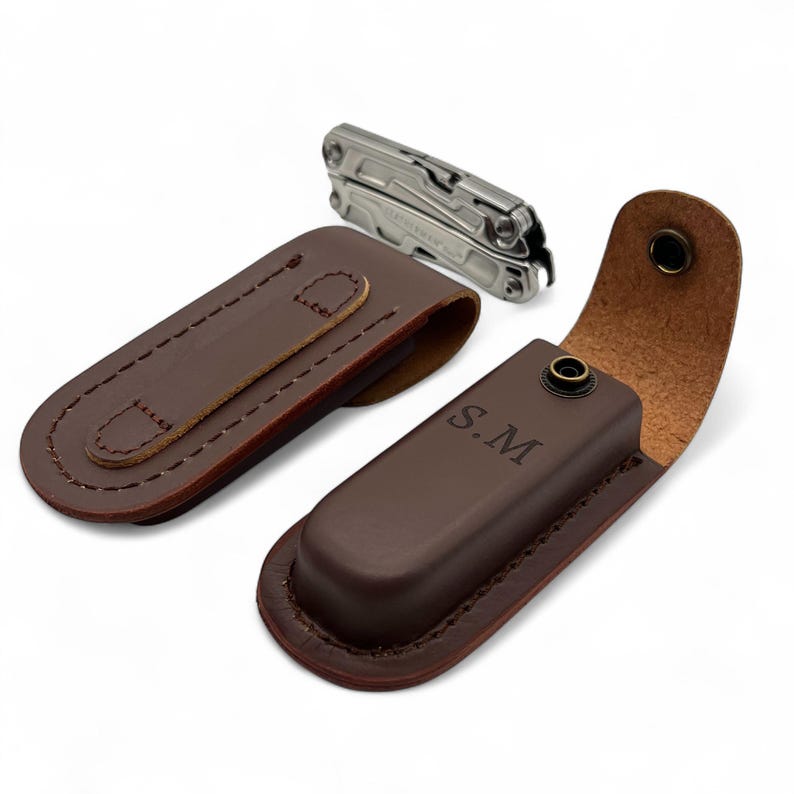 May include: A brown leather multi-tool sheath with a matching multi-tool. The sheath is personalized with the initials "S.M." and has a snap closure. The multi-tool is silver and has multiple tools.