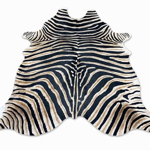 Pode incluir: Um tapete com estampa de zebra com uma forma &uacute;nica. O tapete apresenta listras pretas e bege, com detalhes brancos nas bordas. O tapete foi projetado para se assemelhar a uma pele de zebra e est&aacute; sobre um fundo branco.