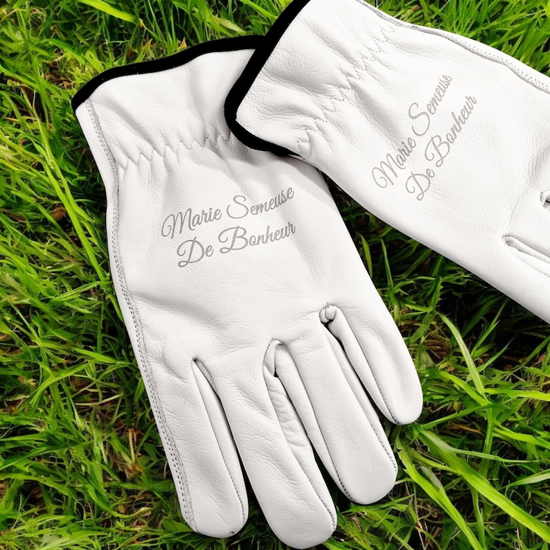 May include: A pair of white leather gloves with black trim. The gloves are embroidered with the text "Marie Semeuse De Bonheur".