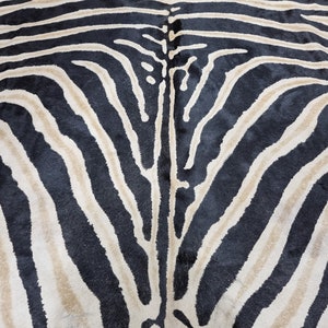 Pode incluir: Close-up de um tapete com listras de zebra. O tapete apresenta listras pretas e bege alternadas, criando um padr&atilde;o animal arrojado. A textura do tapete parece macia e felpuda, adequada para uma sala de estar ou quarto.