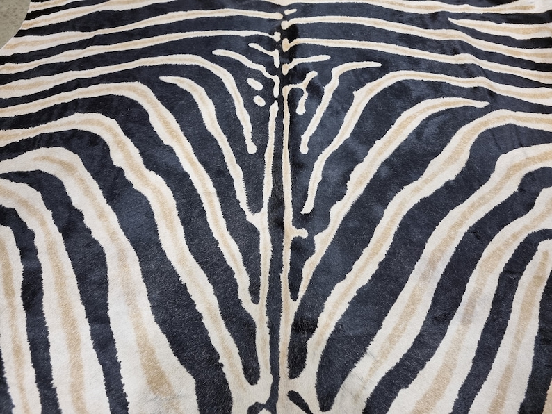 Pode incluir: Close-up de um tapete com listras de zebra. O tapete apresenta listras pretas e bege alternadas, criando um padr&atilde;o animal arrojado. A textura do tapete parece macia e felpuda, adequada para uma sala de estar ou quarto.