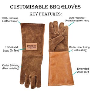 K&ouml;nnte beinhalten: Braune Leder-Grillhandschuhe mit verl&auml;ngertem Handgelenk. Die Handschuhe haben ein Kevlar-Innenfutter und -N&auml;hte f&uuml;r Hitzebest&auml;ndigkeit. Die Handschuhe sind mit einem gepr&auml;gten Logo oder Text personalisierbar. Der Text "DADDY'S BBQ GLOVES" befindet sich auf den Handschuhen.