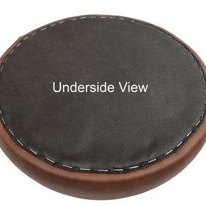 May include: Underside view of a brown round cushion with a black fabric top. The cushion has a stitched edge.