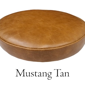 May include: A round, tan leather stool seat. The seat is stitched around the edge and has a slightly distressed look. The text "Mustang Tan" is written below the seat.