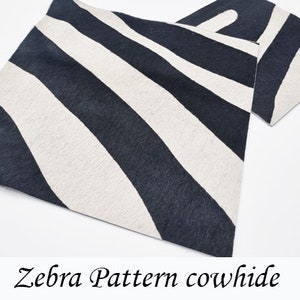 Puede incluir: Una alfombra de piel de vaca con estampado de cebra en blanco y negro. La alfombra está hecha de piel de vaca natural y tiene una sensación suave y lujosa.