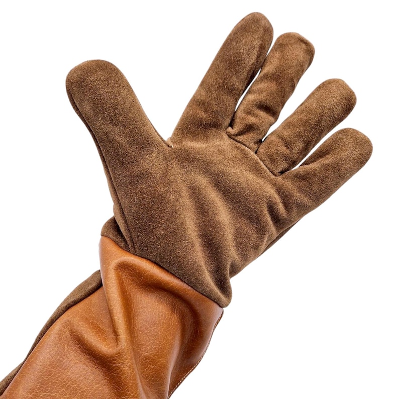 K&ouml;nnte beinhalten: Braune Leder-Arbeitshandschuhe mit langem B&uuml;ndchen. Die Handschuhe haben eine Wildleder-Handfl&auml;che und einen Leder-R&uuml;cken.