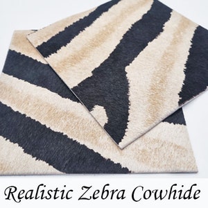 Puede incluir: Dos piezas cuadradas de piel de vaca con un estampado de cebra realista. El diseño presenta rayas negras y beige alternas. El texto "Realistic Zebra Cowhide" está en la parte inferior de la imagen.