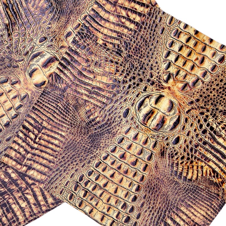 May include: Close-up of a textured, brown and tan faux crocodile leather. The pattern features scales and ridges, creating a realistic reptile skin appearance. The material is likely used for crafting or upholstery.