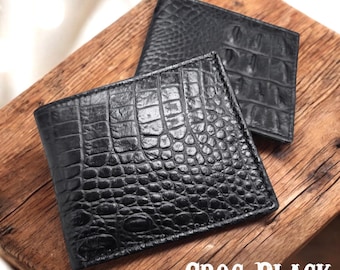 May include: Two black wallets with a crocodile skin texture are shown on a wooden surface. The wallets are rectangular and bi-fold. The text "CROC BLACK" is visible. The wallets have a textured, scaly appearance, with a dark, glossy finish.
