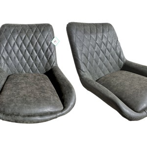 K&ouml;nnte beinhalten: Zwei grau gepolsterte St&uuml;hle mit rautenf&ouml;rmigen Steppn&auml;hten auf den R&uuml;ckenlehnen. Die St&uuml;hle haben geschwungene Armlehnen und ein Used-Finish, das eine Vintage-&Auml;sthetik bietet. Die Sitze sind breit und sehen bequem aus.