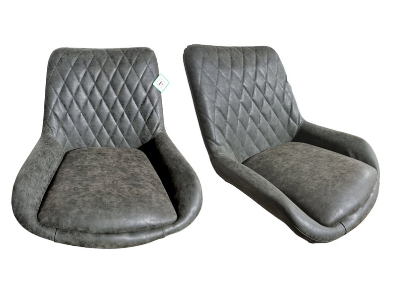 K&ouml;nnte beinhalten: Zwei grau gepolsterte St&uuml;hle mit rautenf&ouml;rmigen Steppn&auml;hten auf den R&uuml;ckenlehnen. Die St&uuml;hle haben geschwungene Armlehnen und ein Used-Finish, das eine Vintage-&Auml;sthetik bietet. Die Sitze sind breit und sehen bequem aus.