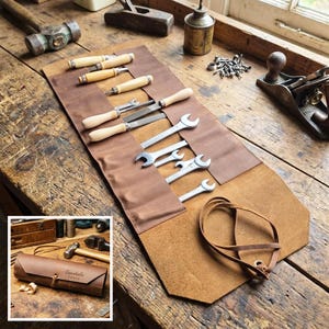 Könnte beinhalten: Eine braune Leder-Werkzeugrolle mit verschiedenen Handwerkzeugen, darunter Meißel und Schraubenschlüssel. Die Rolle ist offen und zeigt die Werkzeuge, die mit einem Lederriemen befestigt sind. Die Werkzeuge sind auf einer Holzoberfläche angeordnet.