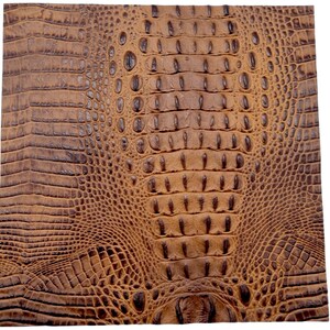 May include: Close-up of a square piece of brown faux crocodile leather. The material has a textured surface with a repeating pattern of scales and ridges, creating a realistic reptile skin appearance.