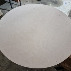 May include: A round, white, wooden tabletop with a natural wood grain pattern.