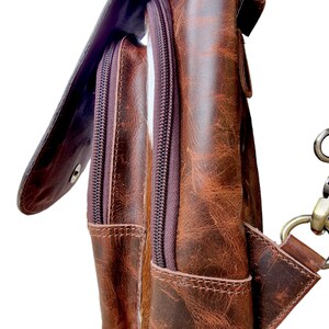 May include: A brown leather satchel with a flap closure and two zippered pockets. The bag has a distressed look and a brown strap.