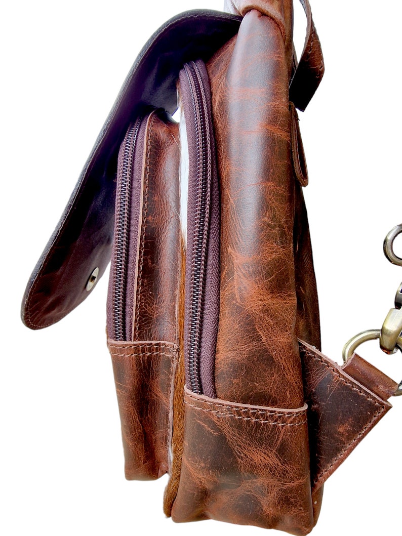 May include: A brown leather satchel with a flap closure and two zippered pockets. The bag has a distressed look and a brown strap.