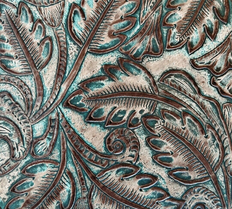 Pu&ograve; includere: Primo piano di una texture in pelle goffrata color verde acqua e marrone con un motivo floreale.