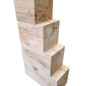 May include: Four wooden blocks stacked on top of each other, each block is slightly smaller than the one below it. The blocks are made of light-colored wood with a natural grain pattern.